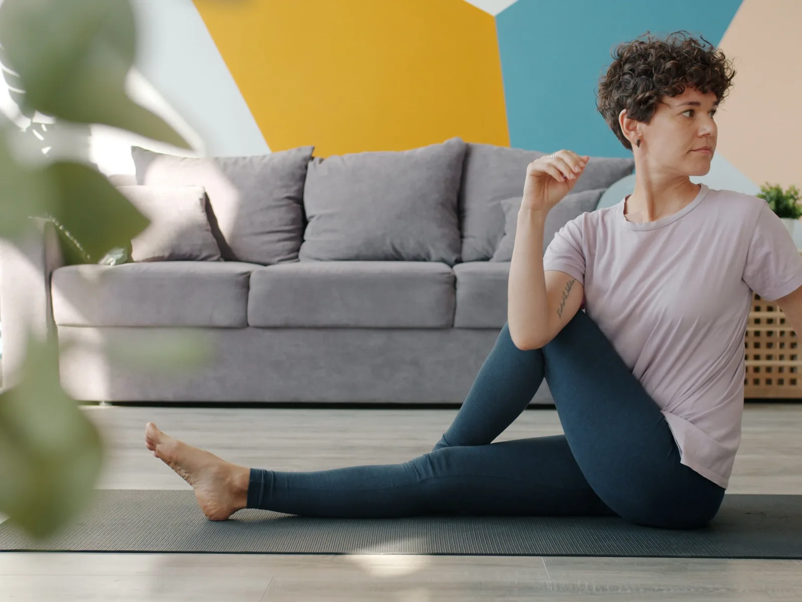 Une personne en tenue de sport prend une posture sur un tapis, dans un salon lumineux.